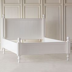 a white bed with wooden posts and headboard in an empty room that has paneled walls