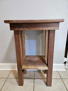 a small wooden table sitting on top of a tile floor next to a white wall