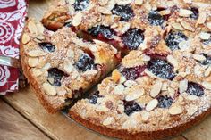 a pie with blueberries and almonds cut into slices on a wooden table next to a red napkin