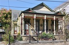 an old house is painted yellow and has red trim on the front porch, along with black iron fence