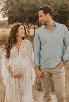 a pregnant couple holding hands and walking through tall grass