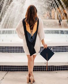 a woman standing in front of a fountain with her back to the camera and holding an umbrella