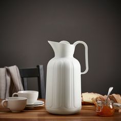 a white pitcher sitting on top of a wooden table next to a cup and saucer