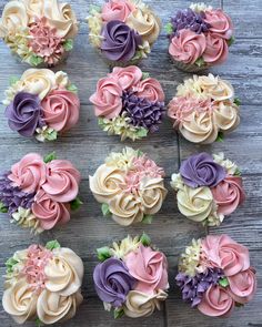 cupcakes decorated with different colored frosting flowers on top of a wooden table