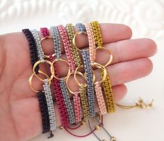 a hand holding several bracelets with gold rings and beads on each one side, all in different colors