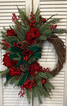 a wreath with red flowers and greenery hanging on a door