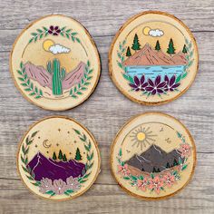 four hand painted wooden coasters with mountains, trees and flowers in the center on a wood background