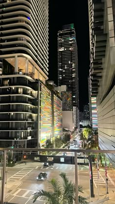 a city street at night with tall buildings and palm trees in the foreground, lit up by brightly colored lights