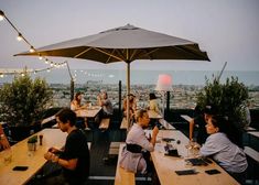 several people sitting at tables with an umbrella over them and the city in the background