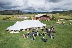 a group of people standing in front of a white tent on top of a lush green field