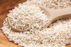 a wooden spoon filled with white seed on top of a table next to a pile of rice