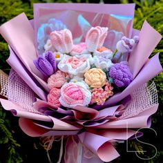 a bouquet of crocheted flowers is shown in front of some greenery with pink ribbon