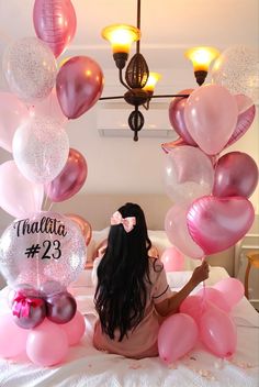 a woman sitting on top of a bed surrounded by balloons