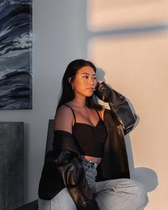 a woman sitting on top of a chair next to a wall holding a black jacket