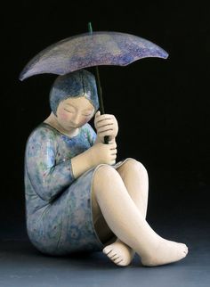 a ceramic figurine sitting on the ground with an umbrella over her head and eyes closed