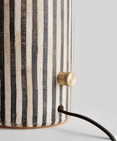 a black and white striped lamp with a gold button on the end that is plugged in