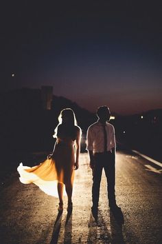 a man and woman are walking down the road at night with their dress blowing in the wind