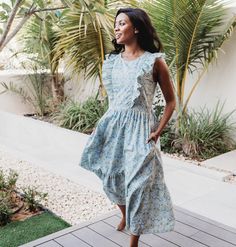 a woman in a blue dress standing on a wooden deck next to some palm trees