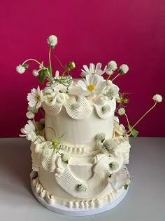 a three tiered white wedding cake with flowers on the top and bottom, against a pink background