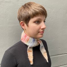 a woman with short hair wearing a multicolored knitted neck scarf against a white wall