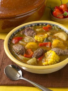 a yellow bowl filled with meat and vegetables on top of a table next to a loaf of bread