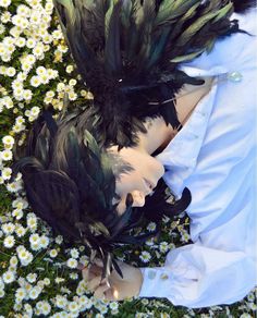 two people are laying in the grass with their faces covered by black and green feathers