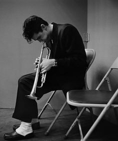 black and white photograph of a man playing the trumpet in a room with chairs around him