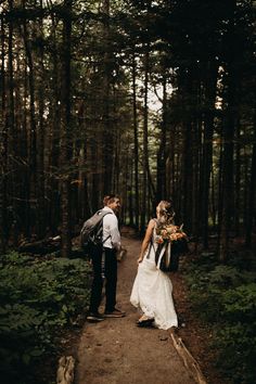 a bride and groom walking through the woods