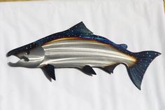 a metal fish on a white sheet with blue and yellow stripes is hanging from the wall