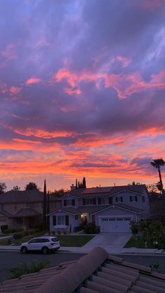 the sky is pink and purple as the sun sets over houses in an area with palm trees