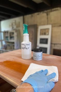 a person wearing blue gloves is cleaning a wooden table with a bottle of water and cloth