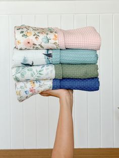 a person holding up a stack of folded towels on top of a wooden table in front of white paneled walls