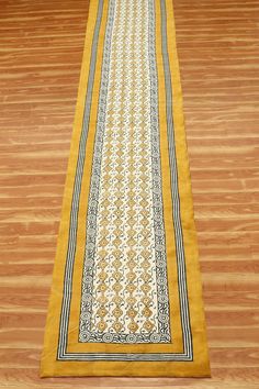 a long yellow runner rug with black and white designs on the bottom, laying on a wooden floor