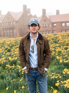 a man standing in front of a field full of yellow daffodils with a building in the background