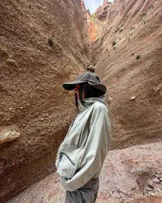 a person wearing a hat and jacket standing in the middle of a canyon with mountains in the background