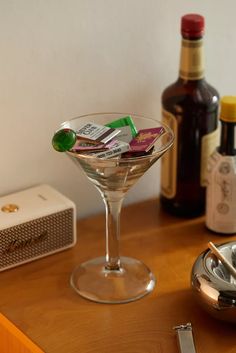 a martini glass sitting on top of a wooden table next to bottles and a spoon