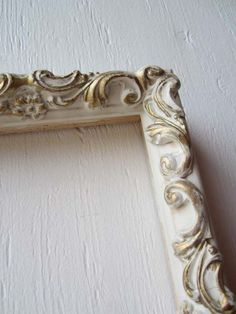 an ornate white and gold frame on the wall