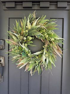 a wreath is hanging on the front door with green leaves and other greenery around it