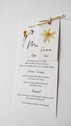 a menu card with flowers on it is attached to a white table cloth and has a string