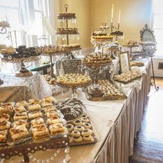 a table topped with lots of desserts and pastries on top of tables next to windows