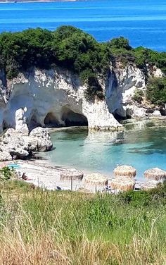 the beach has many umbrellas on it and is surrounded by green trees, grass and blue water