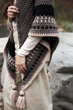 a woman is wearing a crocheted shawl with tassels on it