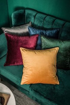 a green velvet couch with four different colored pillows on it's back and side