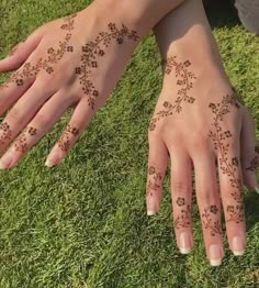 two hands with henna tattoos on them sitting in the grass, one is holding another hand