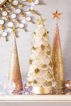 three small christmas trees are sitting on a mantel with gold and white ornaments around them