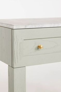 a white wooden table with two drawers and gold knobs on the bottom drawer, against a white background