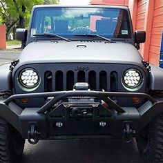 a gray jeep is parked in front of a red building and has its lights on