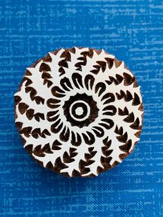 a wooden brooch with black and white designs on the front, sitting on a blue surface