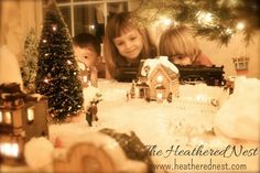 three children are looking at a christmas scene with candles and a train in the snow