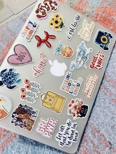 an apple laptop covered in stickers sitting on top of a carpet next to a wall